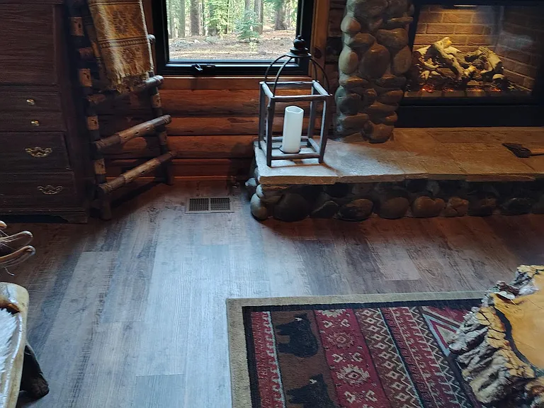 Log-cabin style living area with a stone fireplace, large picture window, and durable flooring for easy everyday living.