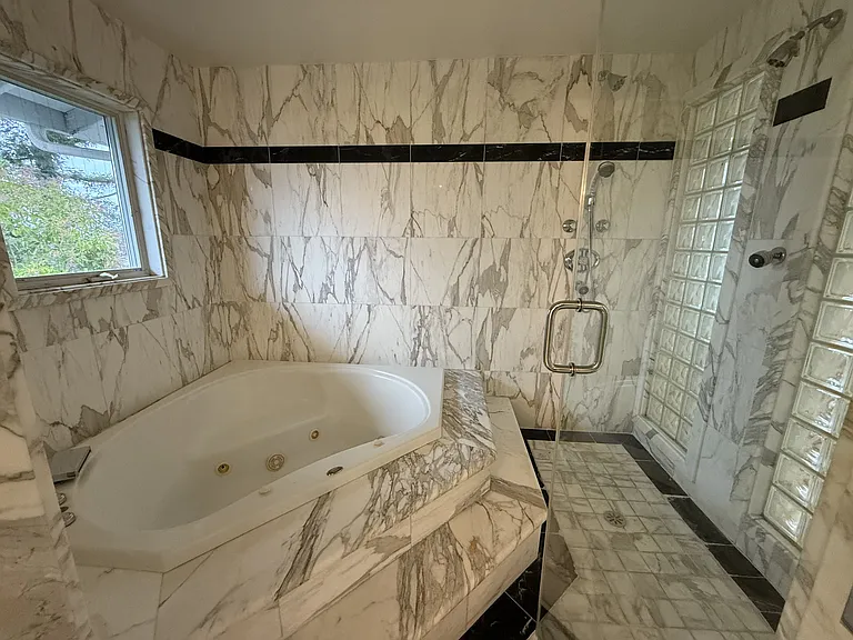 In-suite primary bathroom is tastefully appointed with glass block walls featuring dual sinks, Jacuzzi tub, multi-jet shower stall, a bidet, and a walk-in closet with built-in organized storage.