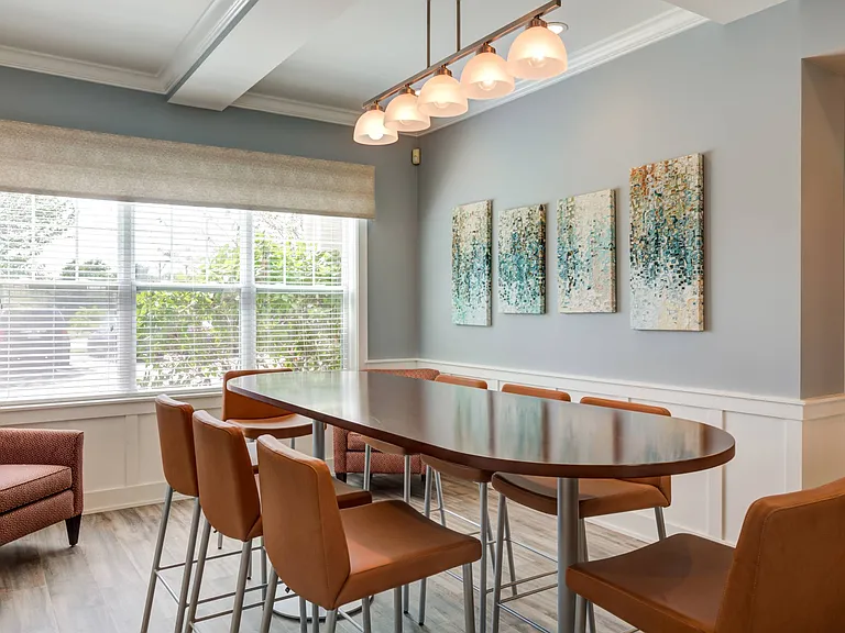 Resident lounge with high-top, oval-shaped table surrounded by stools with chair backs in front of an oversized window at Summit Place apartments in Methuen, MA.
