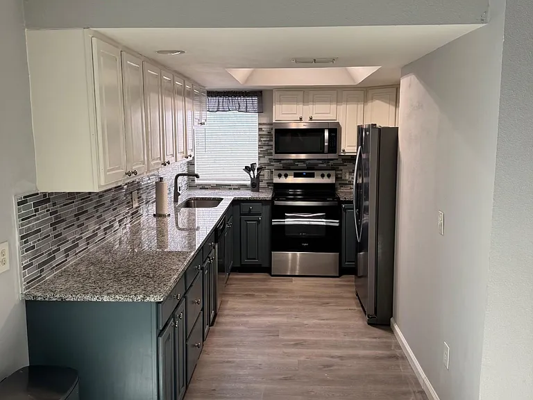 Galley-style kitchen with granite counters, ample cabinetry, mosaic tile backsplash, and stainless steel appliances.