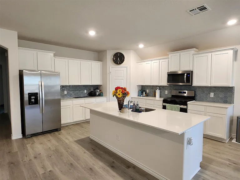 Kitchen featuring a large central island with a sink, white cabinetry, hexagon tile backsplash, stainless steel appliances, and wood-finish flooring