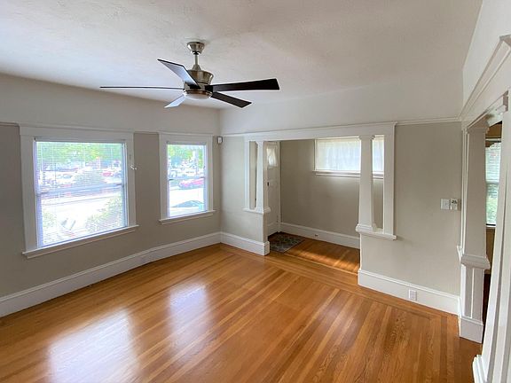 The sunny living room has new blinds on the triple bay windows, remote-controlled ceiling fan, original molding and picture rails