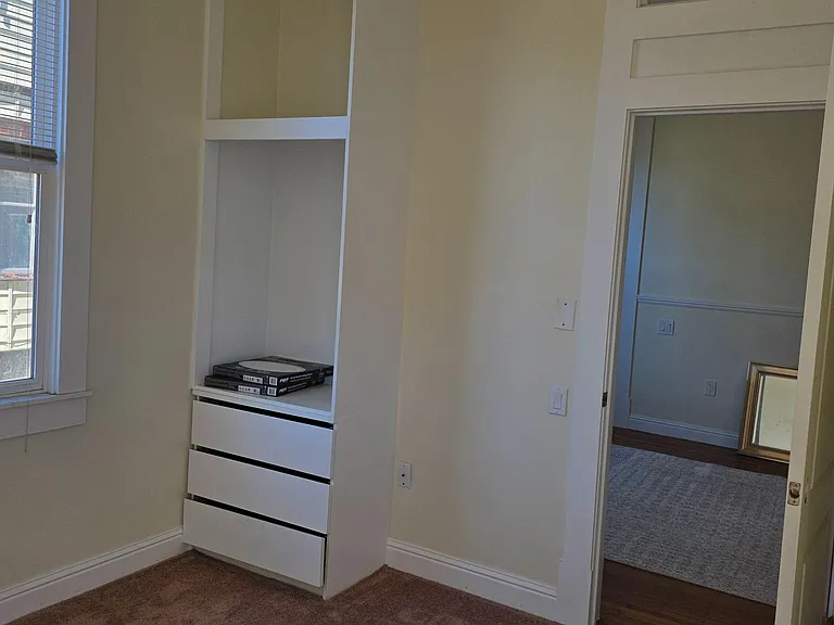 Bedroom nook with a window, built-in shelving and drawers, and easy access to the adjacent room or hallway.