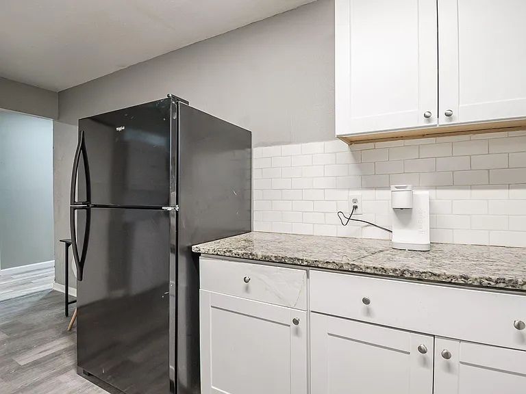 Kitchen features ample cabinet storage, granite-look countertops, subway-tile backsplash, and a full-size refrigerator.