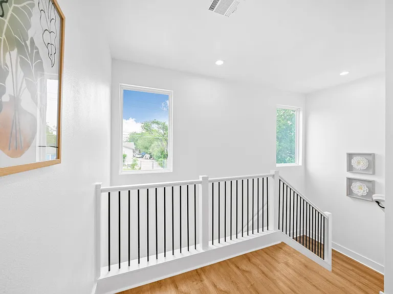 Upstairs landing with wide stairwell, sleek railing, and two large windows offering tree views and natural light.