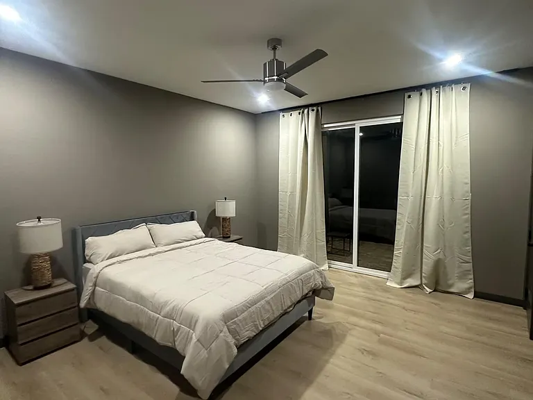 Spacious bedroom with ceiling fan, nightstands, and a sliding glass door framed by full-length curtains.