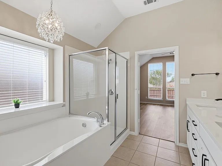 Bathroom featuring a soaking tub, glass-enclosed shower, dual vanity with quartz-like countertops, vaulted ceiling, and a crystal chandelier
