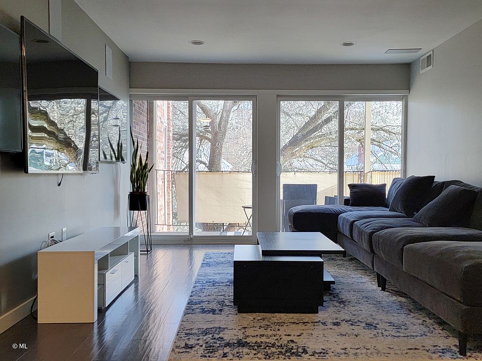 Furnished living room with couch, coffee table, TV console, & 3 large flat screen TVs.
