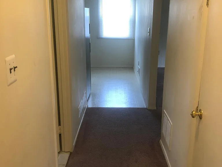 Hallway view from bedrooms into Kitchen. Apartment entrance on right , living room on right and bathroom on left.