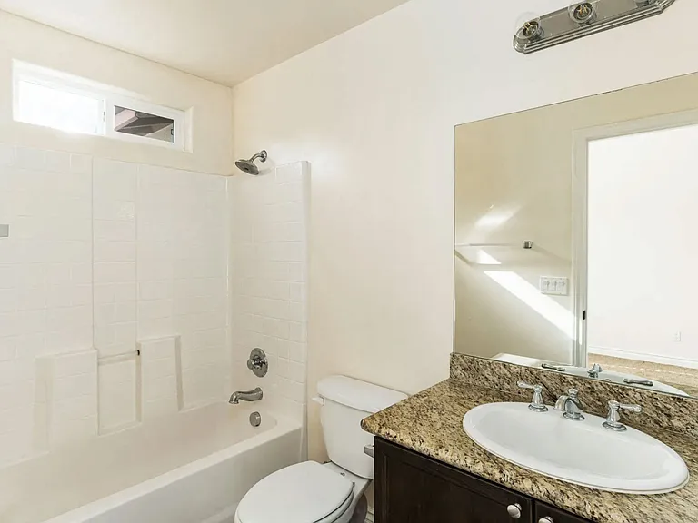 Bathroom with granite slab vanity counter top, white fixtures, upgraded faucets, and privace window for natural light at The Nines Townhomes in Escondido, California.