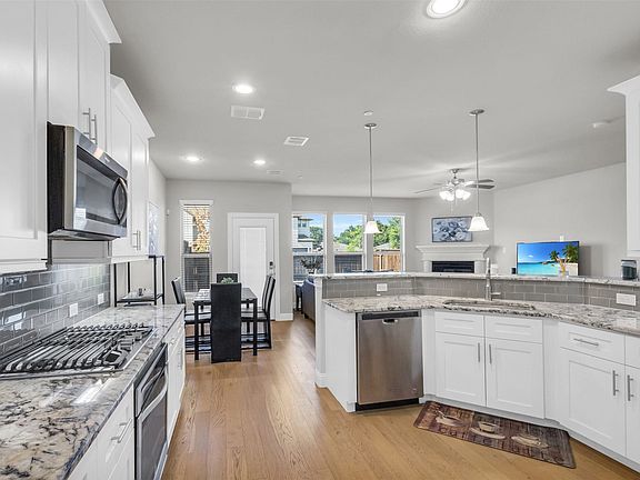 Open-concept kitchen featuring white cabinetry, stainless steel appliances, granite countertops, a subway tile backsplash, and wood-finish flooring