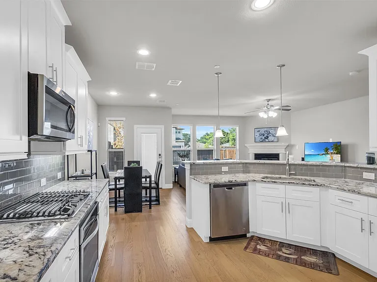 Open-concept kitchen featuring white cabinetry, stainless steel appliances, granite countertops, a subway tile backsplash, and wood-finish flooring
