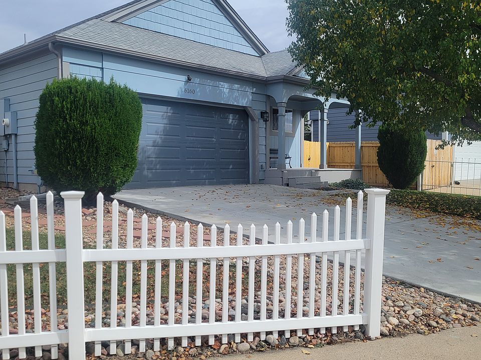 Outdoor view with outdoor lighting, rose bushes and larger shrubs on sides of 2 car attached garage.