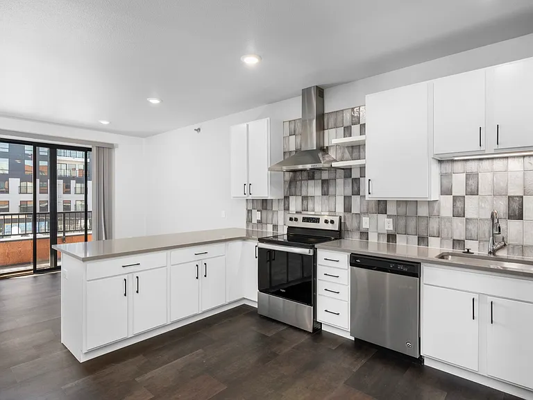 Modern kitchen with sleek white cabinetry, stainless steel appliances, and stylish tiled backsplash in a bright apartment space with large glass doors. Modern kitchen with sleek white cabinetry, stainless steel appliances, and stylish tiled backsplash in