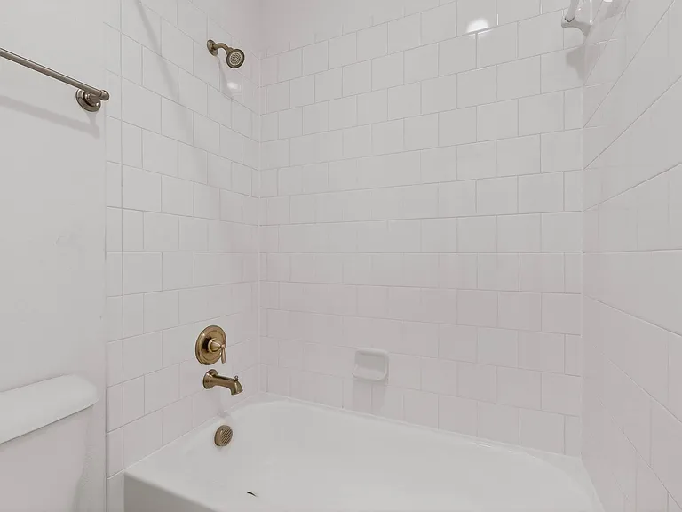 A bright white bathroom featuring a bathtub, toilet, and shower