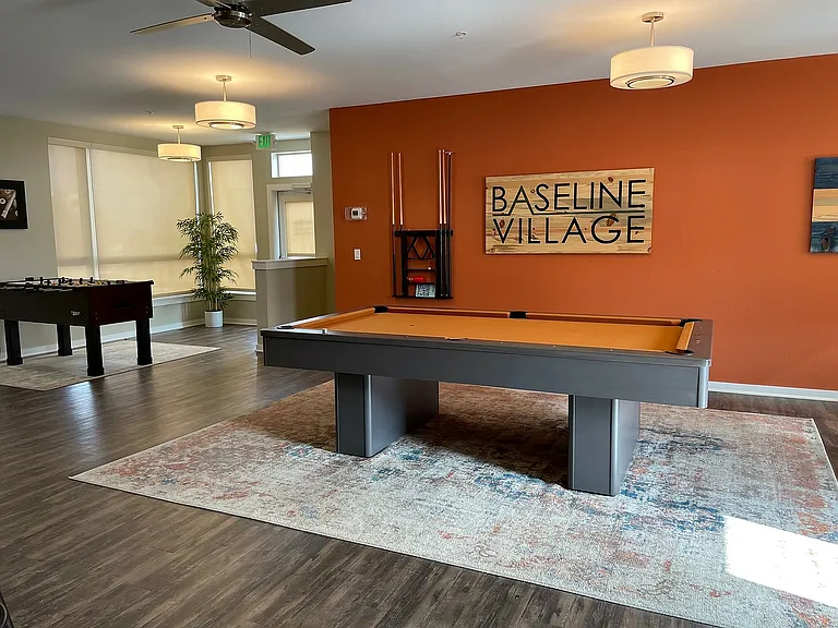 Chic and inviting game room at Baseline Village featuring a sleek pool table and foosball table, accented by modern lighting and warm decor.