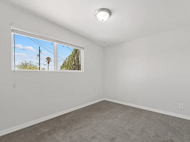 Sunny second bedroom with a large window bringing in natural light.