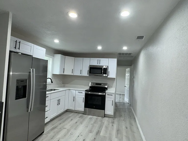 Updated galley kitchen with white shaker cabinets, ample counter space, and stainless-steel refrigerator, range, and microwav