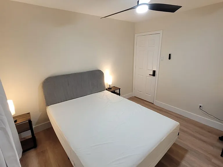Furnished bedroom with a full bed, nightstands, and ceiling fan, plus durable flooring and a clean, simple layout.