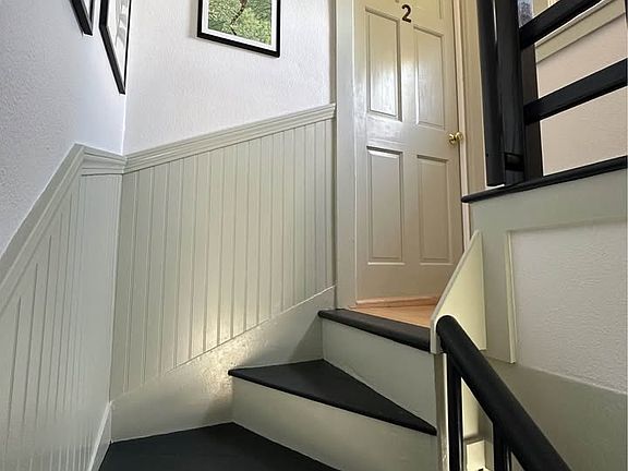 The front door to apartment #2 is located at the top of the stairs. The landing is bright with a window. There is a door opposite that leads to the walk-up attic storage area.