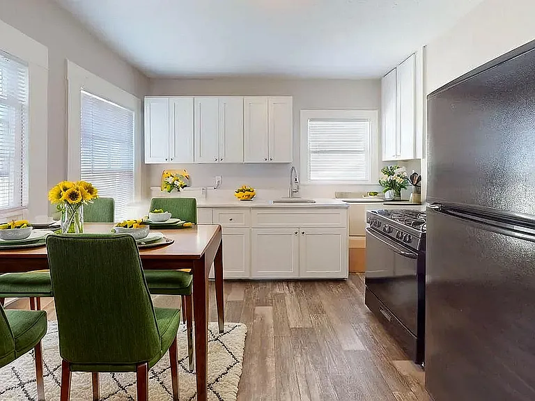 Bright and modern kitchen and dining area featuring elegant white cabinets, a sleek black refrigerator, and vibrant green chairs with a touch of sunflower decor.