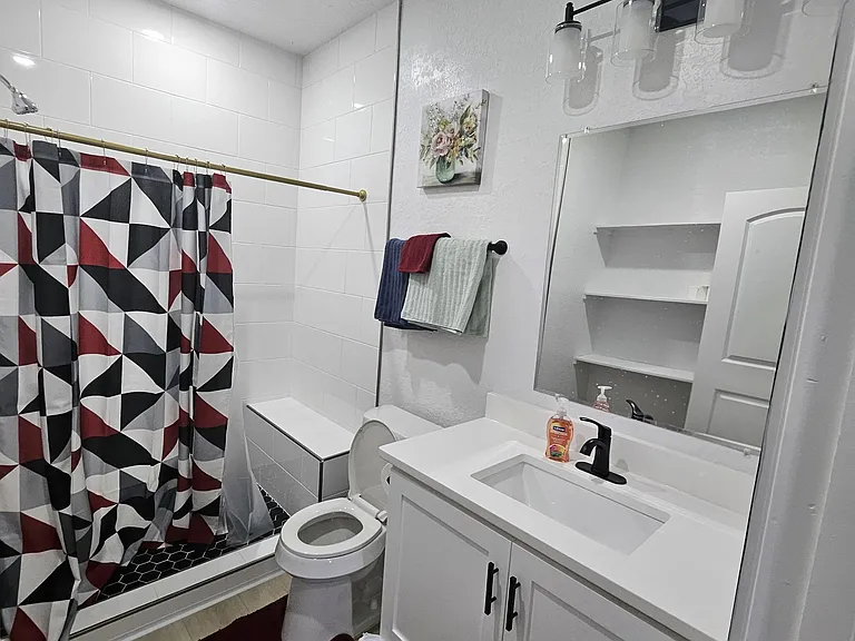 Private full bath with a tiled shower and updated vanity with storage, and built-in shelving for linens.