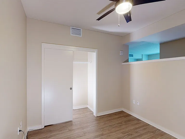 Spacious apartment bedroom with large closet and wood-style flooring.