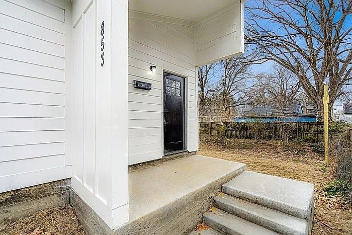 A contemporary entrance defined by sharp architectural angles, crisp white horizontal siding, and a contrasting dark wood door.