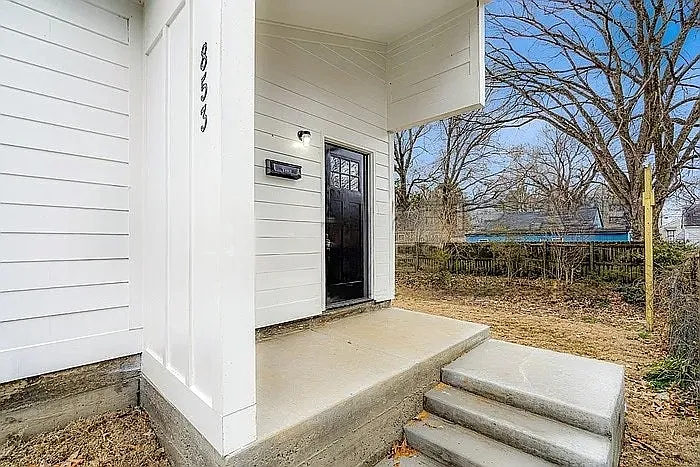 A contemporary entrance defined by sharp architectural angles, crisp white horizontal siding, and a contrasting dark wood door.