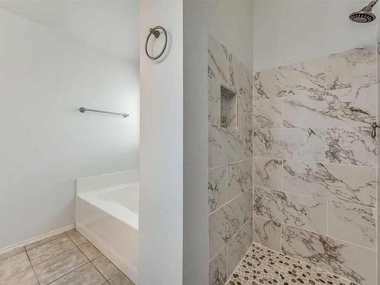 Shower stall featuring large format marbled wall tiles, a built-in niche, and pebble-style floor tiling