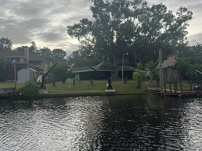 Waterfront backyard setting with mature shade trees and open lawn, plus dock access for enjoying the water views.