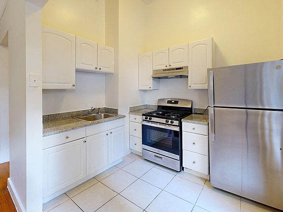 Kitchen with multiple cabinets, refrigerator, stove, range hood, and sink