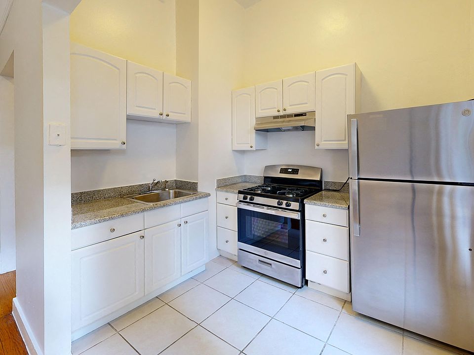Kitchen with multiple cabinets, refrigerator, stove, range hood, and sink