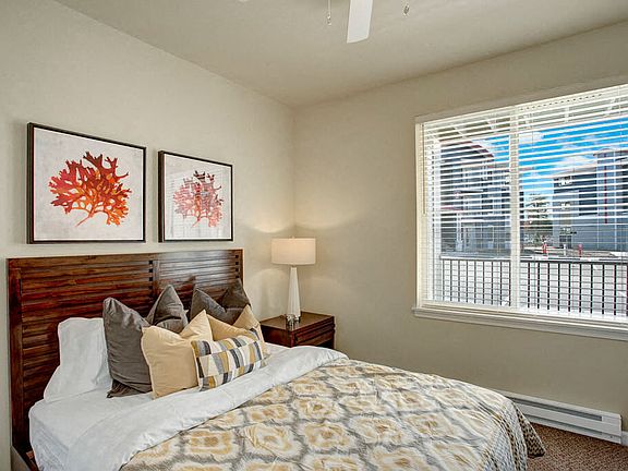 A bedroom with a large window looking out to the patio and the rest of the property with a bed, nightstand, and ceiling fan