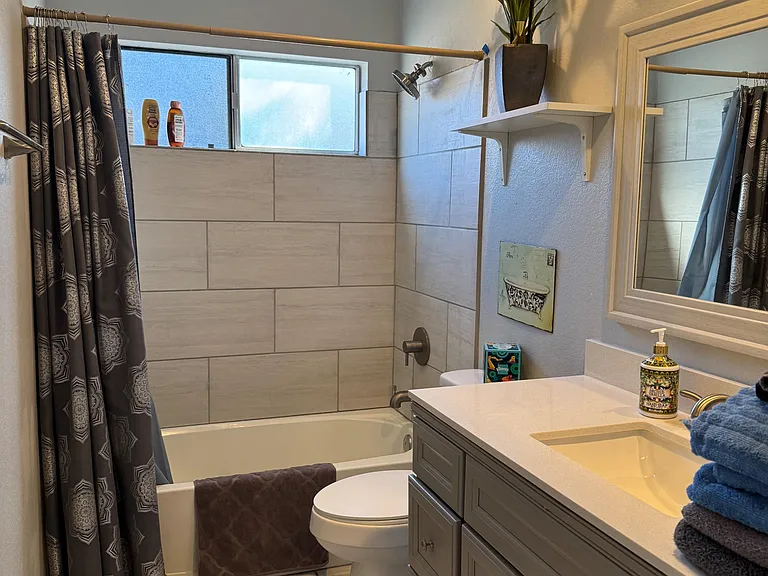 Updated full bath with tiled tub/shower surround, single-sink vanity with storage, and a window for ventilation.