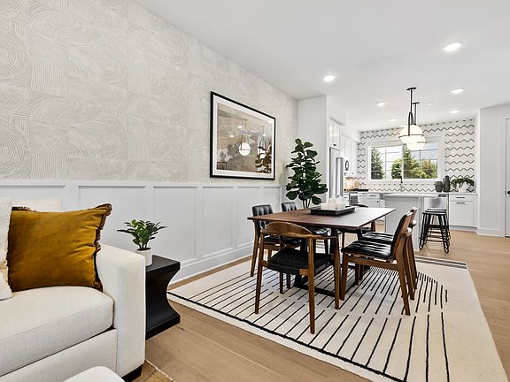 A modern and minimalist dining area with a white sofa, a wooden dining table and chairs, and various