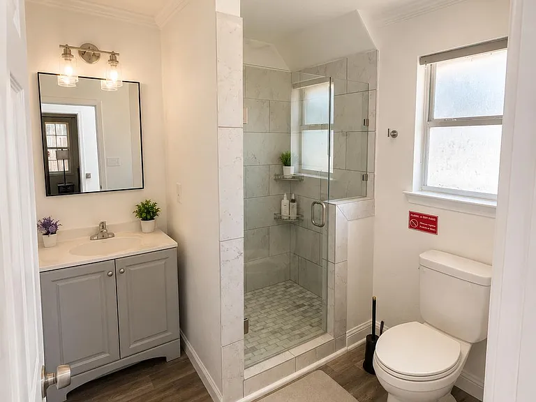 Updated bathroom with a glass-enclosed tile shower, single-sink vanity with storage, and a window for natural light.