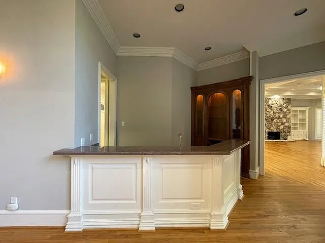 Kitchen with light wood-type flooring, ornamental molding, dark stone counters, a stone fireplace, and a peninsula