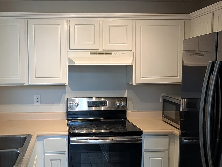 Clean kitchen layout with glass-top electric range, modern track lighting, and fresh white cabinets