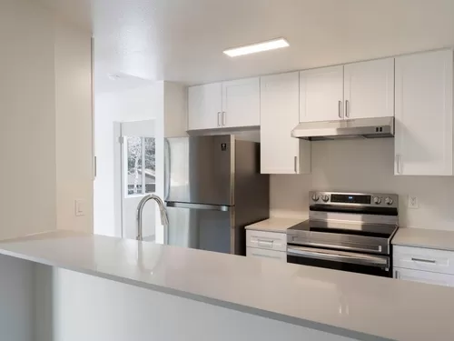 Renovated Package I kitchen with stainless steel appliances, light grey quartz countertops, and new white cabinetry - eaves Mission Viejo