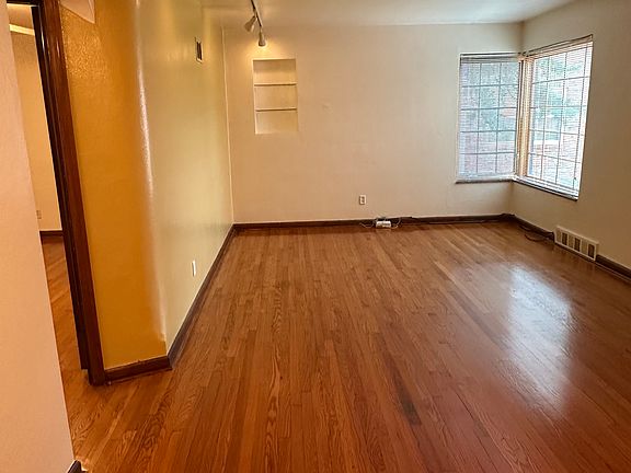Combined dining room and living room seen from kitchen. Front windows look onto gardens and street