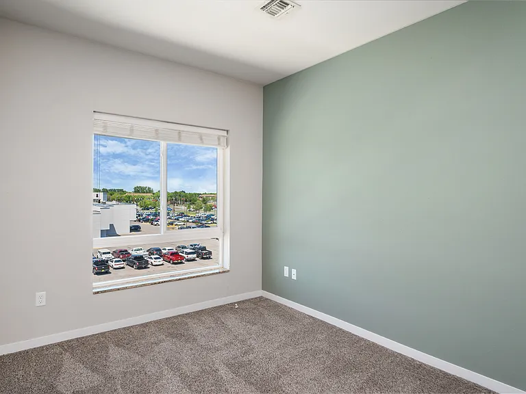 Bright, sunlit room with a large window showcasing a vibrant view of a parking area and greenery beyond. Bright, sunlit room with a large window showcasing a vibrant view of a parking area and greenery beyond.
