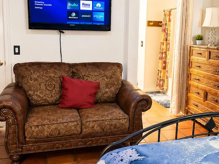Spacious bedroom suite with a comfortable seating area, wall-mounted TV, and convenient access to the nearby bath area.