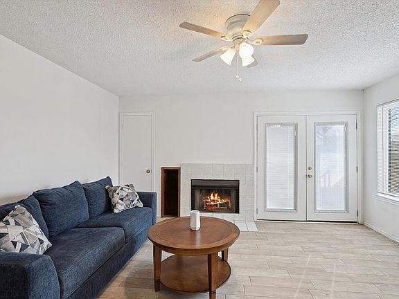 Living area with ceiling fan, a textured ceiling, french doors, light wood-type flooring, and a fireplace