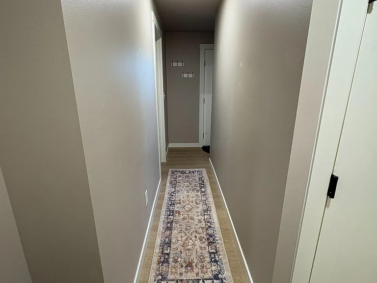 Long hallway with durable wood-look flooring, overhead recessed lighting, and wall hooks for everyday storage.