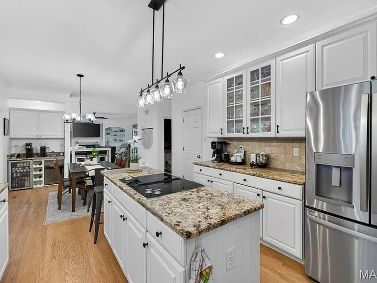 Well-appointed kitchen featuring a center island cooktop, stainless steel appliances, white cabinetry, and granite countertops