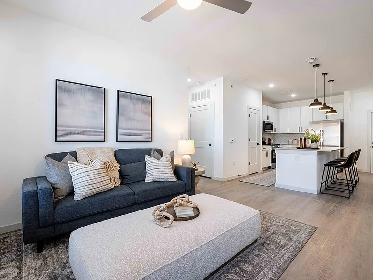 This open concept living area in the Garrett Parker B1 floor plan flows directly into a kitchen with island seating for three and a stainless steel refrigerator.