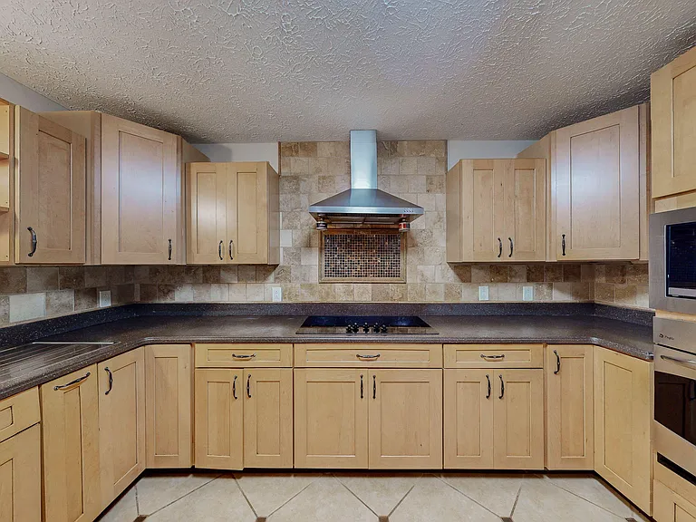 Spacious kitchen with ample cabinet storage, tile backsplash, smooth cooktop, and a stainless vent hood for everyday cooking.