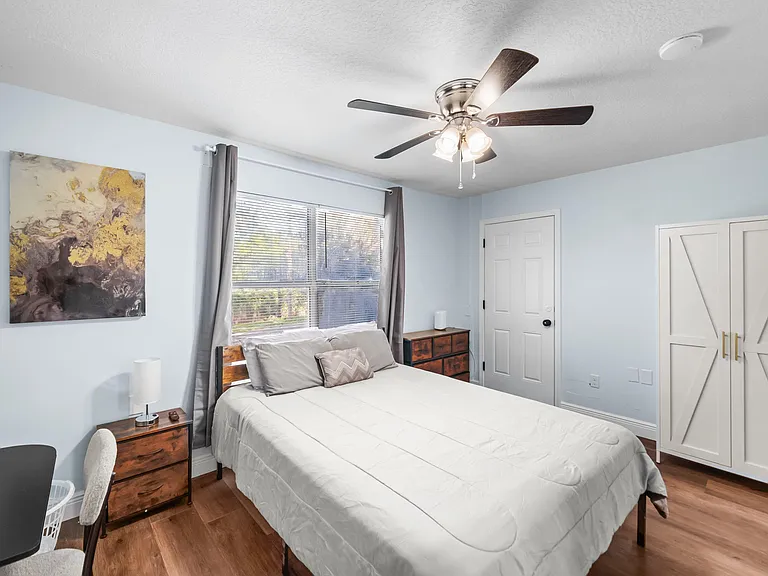 Bedroom with a queen bed, large window with drapes, ceiling fan light, and wardrobe plus dresser for ample storage.