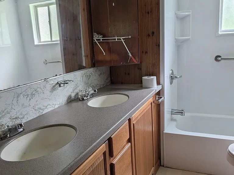 Large vanity in bath with double sinks, double medicine cabinets, mirrored wall, newer shower/ tub insert with window.